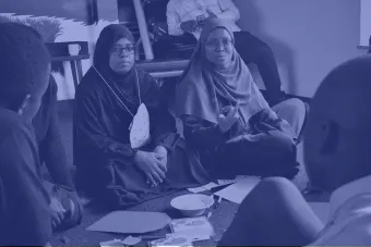 two teachers wearing hijabs sit on the ground during a workshop with Katie Krummeck and Gray Garmon