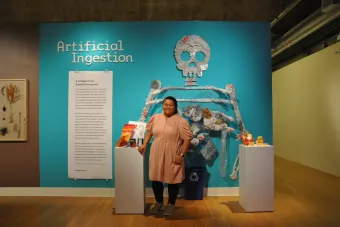 2022 MFA Design graduate Vanessa Diamos posing next to her exhibition Artificial Ingestion