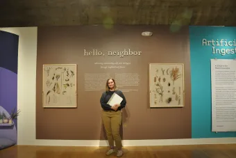 2022 MFA Design graduate Kristen Graham posing next to her exhibition Hello Neighbor