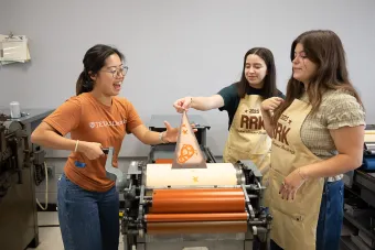 Students pull a penant from a printing press in the design lab