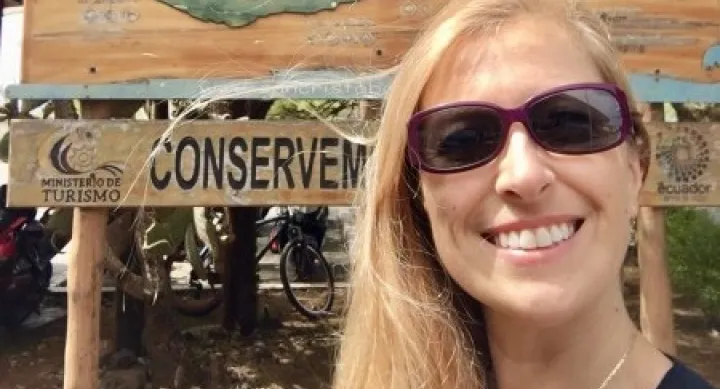 Natacha Poggio smiles in front of a sign that reads "Welcome to San Cristobal"