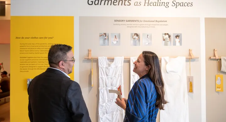 Two people laughing as they observe MFA design 2023 exhibit Garments as Healing Spaces at The University of Texas at Austin